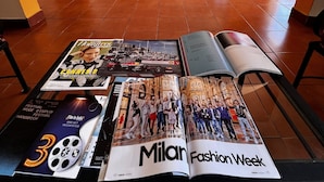 Une pièce spacieuse avec un sol carrelé, un canapé rouge, une porte en bois et un magazine ouvert sur une table.