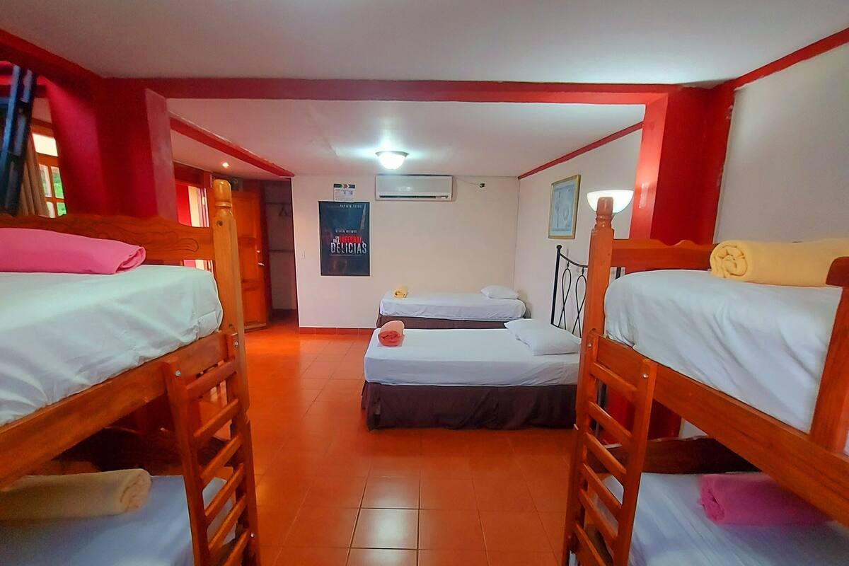 Une chambre de dortoir avec quatre lits superposés, un sol carrelé, une affiche au mur et un appareil de climatisation.