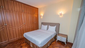 Ein Schlafzimmer mit großem Holzschrank, einem Bett mit weißer Bettwäsche, zwei Nachttischen und Wandleuchten.