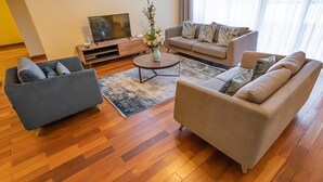 Ein modernes Wohnzimmer mit grauem Sofa, beigem Sofa, Couchtisch und Flachbildfernseher auf einem Holzboden.