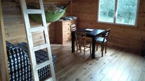 Interno di una baita con letto a soppalco, un tavolo da pranzo con sedie, una finestra vista alberi e pavimento in legno.