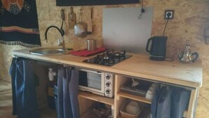 Cucina compatta con piano cottura a gas, lavello e forno a microonde. Pentole e bollitore sono appesi a parete.