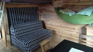 Interno accogliente di una baita con un divano a quadri, un'amaca verde e una tenda a righe.