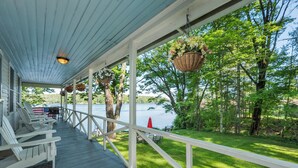 A covered porch with white railings, outdoor seating, and hanging flower baskets. - Nostalgic Winter Harbor Wonderland on Lake Winnipesaukee Sleeps 16 (Tuftonboro)