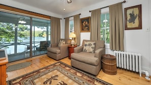 A cozy living room with two sofas, a wooden coffee table, a lamp, and a view of a lake through large windows. - Nostalgic Winter Harbor Wonderland on Lake Winnipesaukee Sleeps 16 (Tuftonboro)