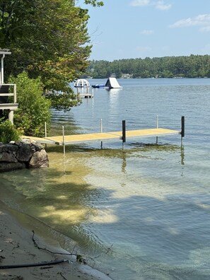 A wooden dock extending into a calm lake, surrounded by trees and a stone wall. - Nostalgic Winter Harbor Wonderland on Lake Winnipesaukee Sleeps 16 (Tuftonboro)