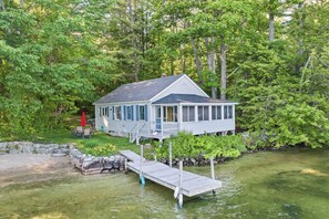 A house with a dock extending into a body of water, surrounded by dense greenery. - Nostalgic Winter Harbor Wonderland on Lake Winnipesaukee Sleeps 16 (Tuftonboro)