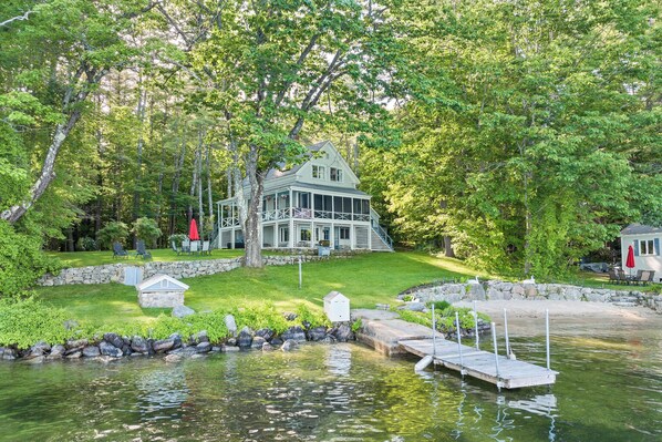 A lakeside house with a dock, a grassy lawn, and a stone wall. - Nostalgic Winter Harbor Wonderland on Lake Winnipesaukee Sleeps 16 (Tuftonboro)