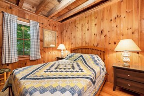 A wooden-paneled bedroom with a bed, two bedside lamps, a window with curtains, and a mirror. - Nostalgic Winter Harbor Wonderland on Lake Winnipesaukee Sleeps 16 (Tuftonboro)