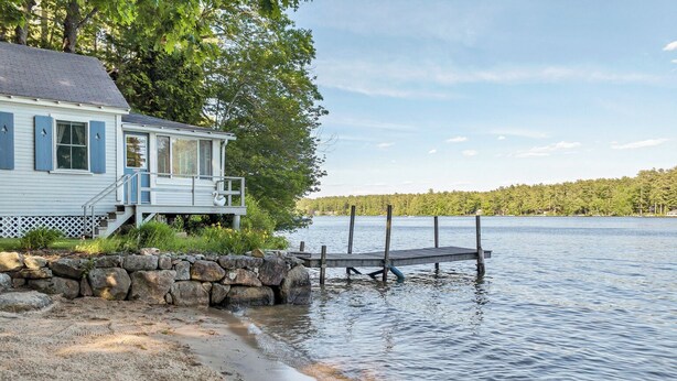 A lakeside cabin with a dock extending into the water, surrounded by trees and a stone wall. - Nostalgic Winter Harbor Wonderland on Lake Winnipesaukee Sleeps 16 (Tuftonboro)