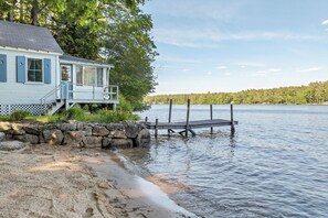 A lakeside cabin with a dock extending into the water, surrounded by trees and a stone wall.