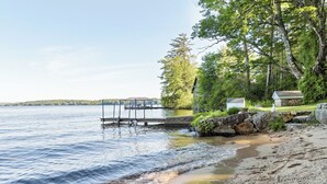 A lakeside scene with a dock extending into calm waters, surrounded by trees and a small building. - Nostalgic Winter Harbor Wonderland on Lake Winnipesaukee Sleeps 16 (Tuftonboro)