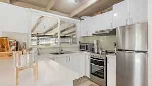A modern kitchen with white cabinetry, a stainless steel refrigerator, a microwave, a coffee maker, and a large window with blinds. - Amongst The Ti-Trees - Rye (Rye)