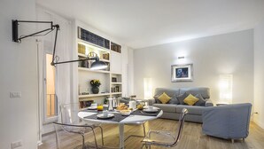 Ein modernes Wohnzimmer mit Essbereich, einem grauen Sofa, einem Couchtisch und einem Bücherregal voller Bücher.