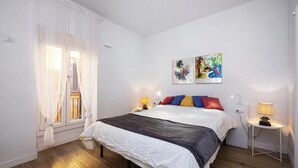Ein Schlafzimmer mit einem Bett, zwei Nachttischlampen, einem Fenster mit Vorhängen und zwei Wandbildern.
