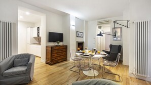 Ein modernes Wohnzimmer mit Essbereich, Holzböden, einem grauen Sofa, einem Holzschrank, einem Flachbildfernseher und einem Kamin.