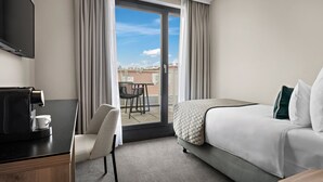 Ein Hotelzimmer mit einem Bett, einem Schreibtisch mit Kaffeemaschine, einem Sessel und einem Fernseher.