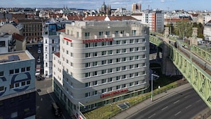 Ein mehrstöckiges Hotel mit einem gut sichtbaren 'Leonardo Hotels'-Schild, umgeben von Stadtgebäuden und einer Grünbrücke.
