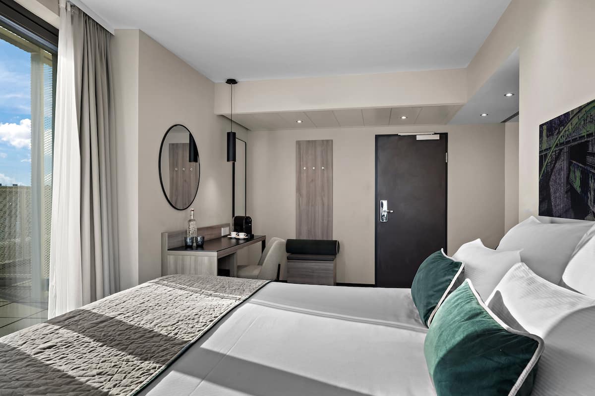 A modern hotel room with a large bed, a desk, a chair, a mirror, and a door.