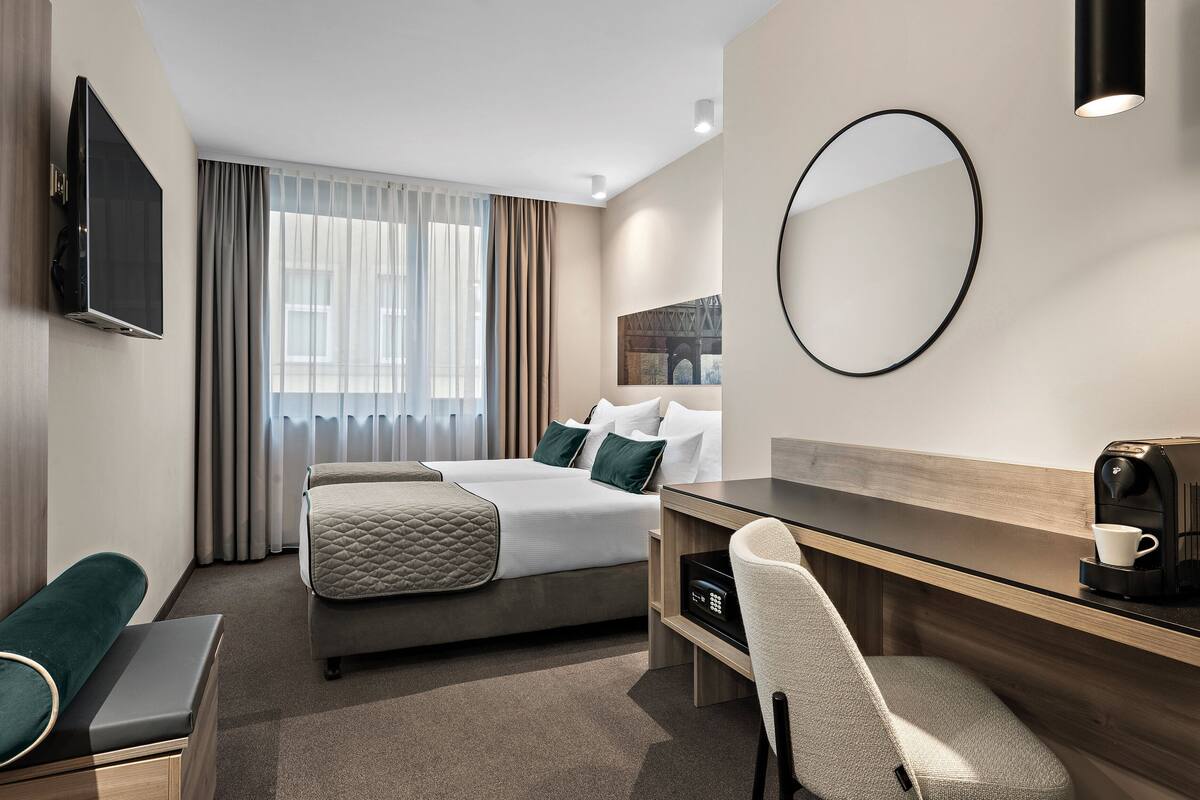 A modern hotel room with a bed, a desk, a chair, a TV, and a coffee machine.