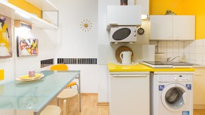 Cocina compacta con microondas, lavadora y un pequeño comedor con mesa y sillas.