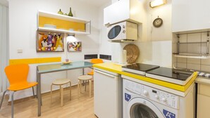 Una cocina compacta con microondas, lavadora y un pequeño comedor con mesa y sillas.