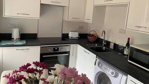 Uma cozinha moderna com armários brancos, forno embutido, lava-louças, pia e máquina de lavar roupa.