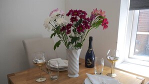 Mesa de jantar posta com pratos brancos, copos de vinho, um vaso com flores e uma garrafa de champanhe.