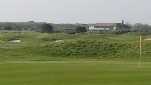 Um campo de golfe com um clube de campo ao fundo.