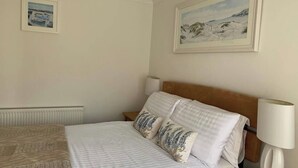 Quarto com cama, almofadas, mesa de cabeceira, luminária, radiador e duas fotos emolduradas na parede.