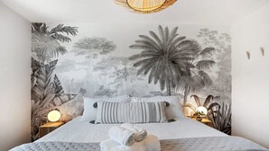 A bedroom with a large bed, a mural of tropical foliage on the wall, and two bedside lamps. - Marbella Lane - 3BR Designer Home in Pacifica (Pacifica)