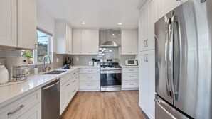 A modern kitchen with white cabinets, stainless steel appliances, and a wooden floor. - Marbella Lane - 3BR Designer Home in Pacifica (Pacifica)
