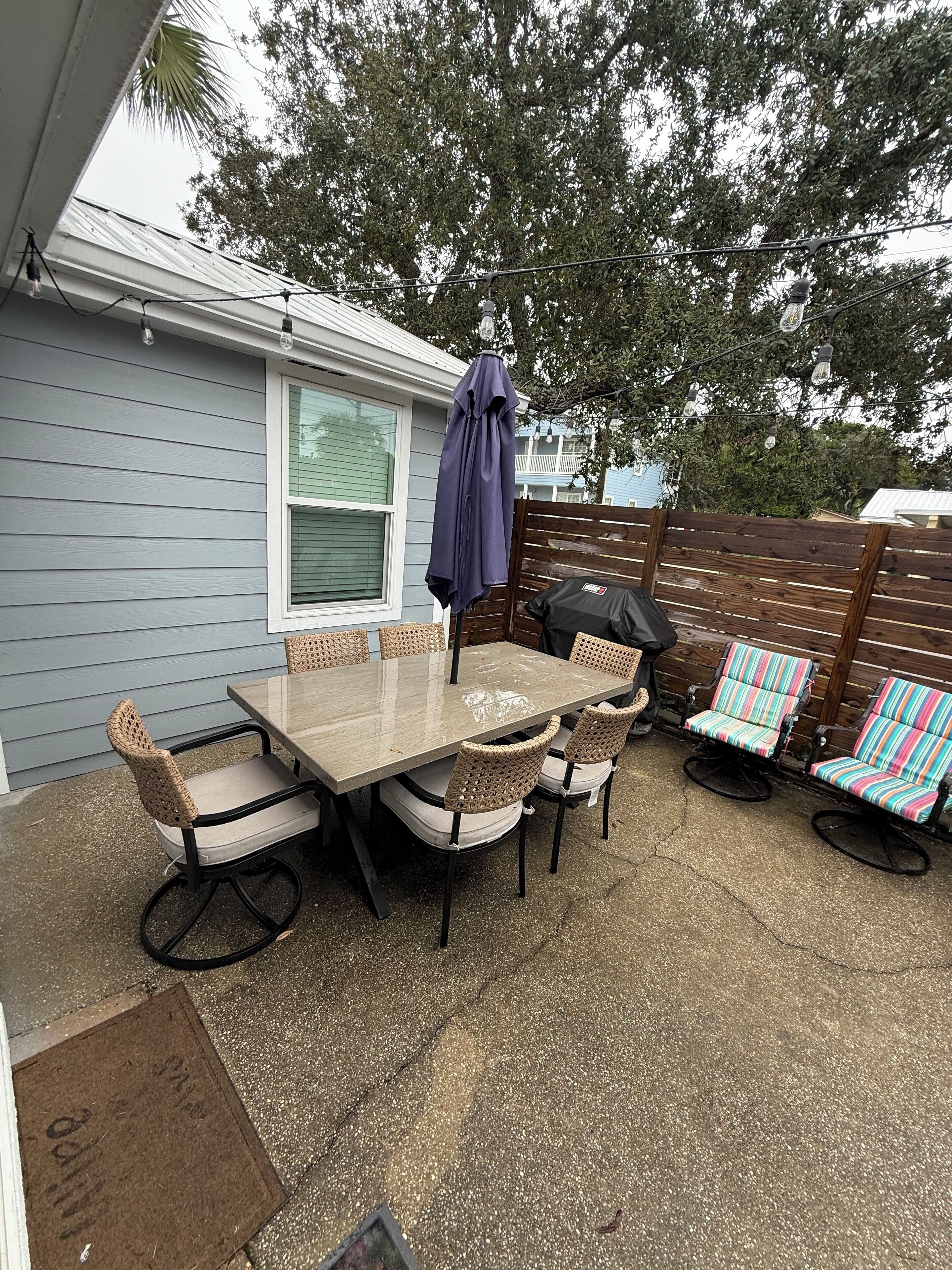 Une terrasse avec une table et des chaises, un barbecue et une clôture en bois.
