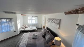 A bedroom with a large bed, a smaller bed, a bedside table with a lamp, and a window with curtains.