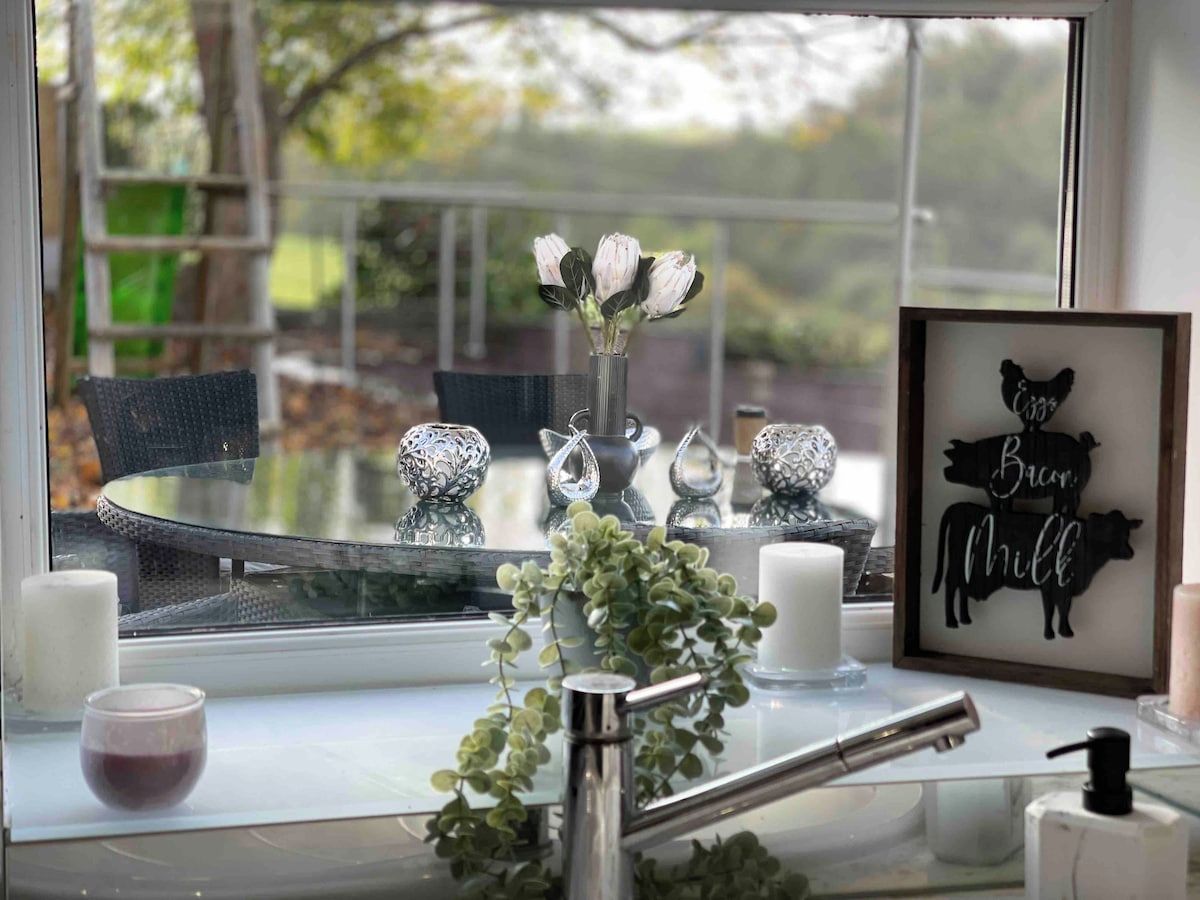 A kitchen counter with a vase of flowers, a framed picture, and a window with a view of trees.
