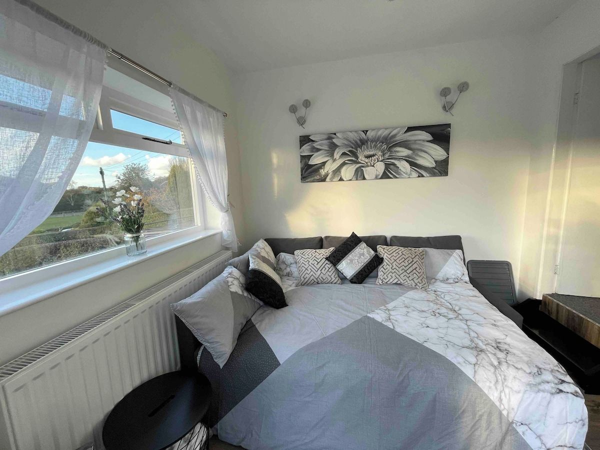 A bedroom with a bed, a window with curtains, a radiator, and a wall-mounted artwork.