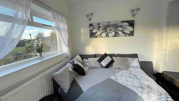 A bedroom with a bed, a window with curtains, a radiator, and a wall-mounted artwork.