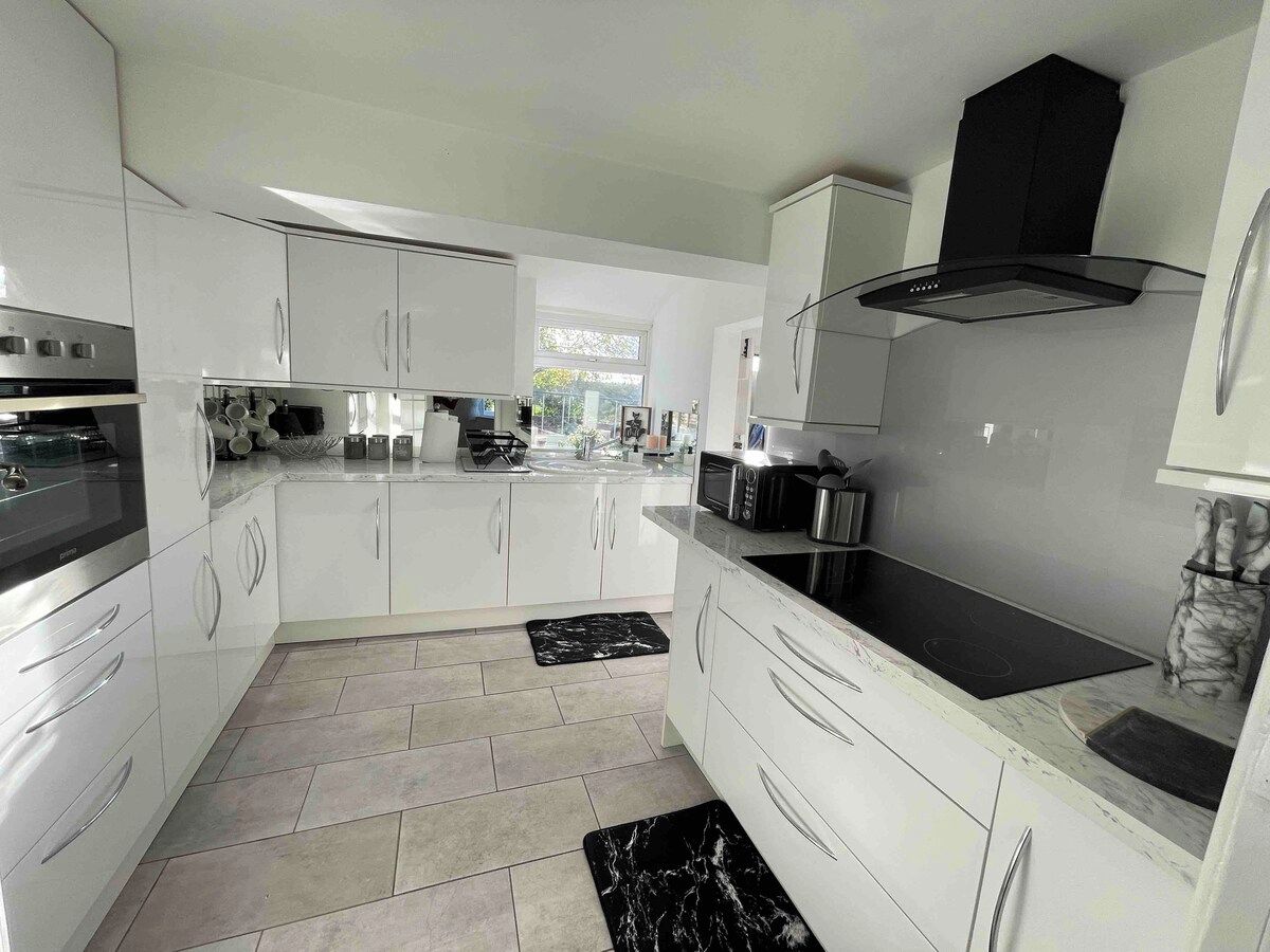 A modern kitchen with white cabinetry, a black induction cooktop, and a stainless steel range hood.