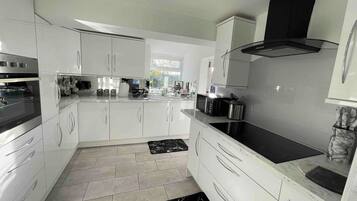 A modern kitchen with white cabinetry, a black induction cooktop, and a stainless steel range hood.