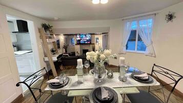 A dining area with a table set for four, a television in the background, and a window with curtains.