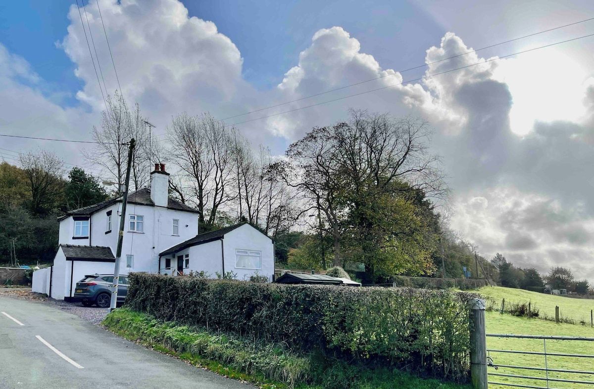 A white house with a garage, a hedge, and a grassy field.