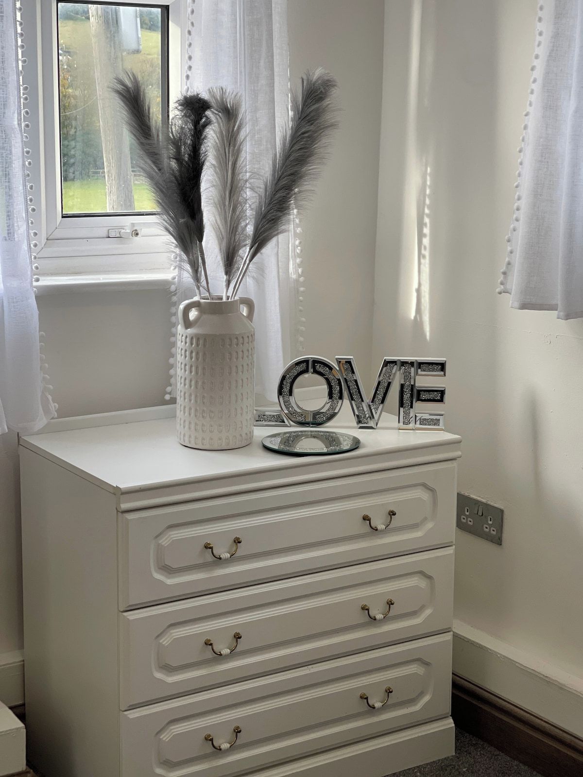 A white dresser with three drawers and a vase with feathers.
