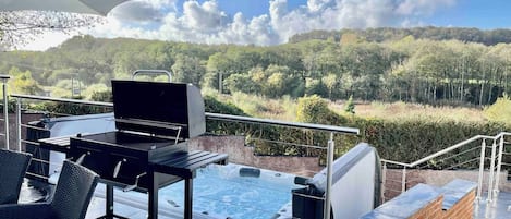 Un patio exterior con un jacuzzi, una parrilla y mobiliario de mimbre.
