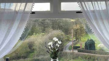 A window with sheer curtains, a vase with flowers, and a view of a landscaped garden.