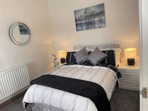 Une chambre à coucher avec un lit, des tables de chevet, un miroir, une lampe et un tableau au mur.