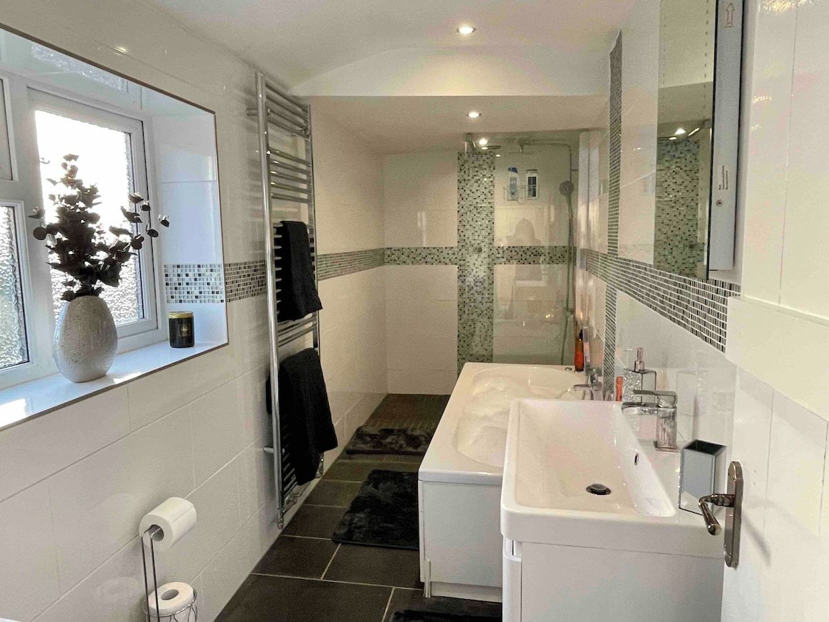 Un baño moderno con un espejo grande, un lavamanos blanco y una zona de ducha.
