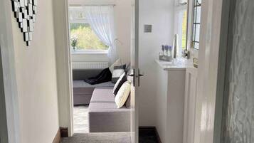 A hallway leading to a bedroom with a bed, a window with curtains, and a wall-mounted mirror.