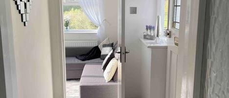 Un pasillo que conduce a un dormitorio con cama, ventana con cortinas y un espejo montado en la pared.
