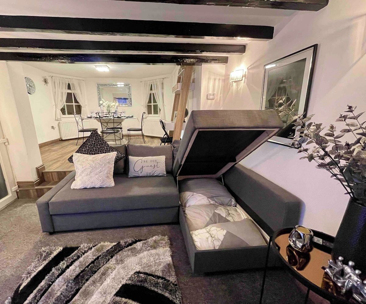A modern living room with a sectional sofa, a dining area in the background, and a decorative plant on the right.