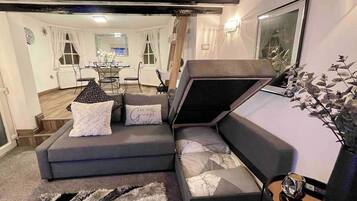 A modern living room with a sectional sofa, a dining area in the background, and a decorative plant on the right.